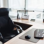 Workplace of businessman: computer, wooden table and chair in cabinet. Office style. Modern equipment and objects. Spacious cabinet of business person.